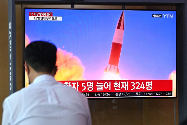 Back of a man's head in the foreground and a TV showing a missile launch in the background
