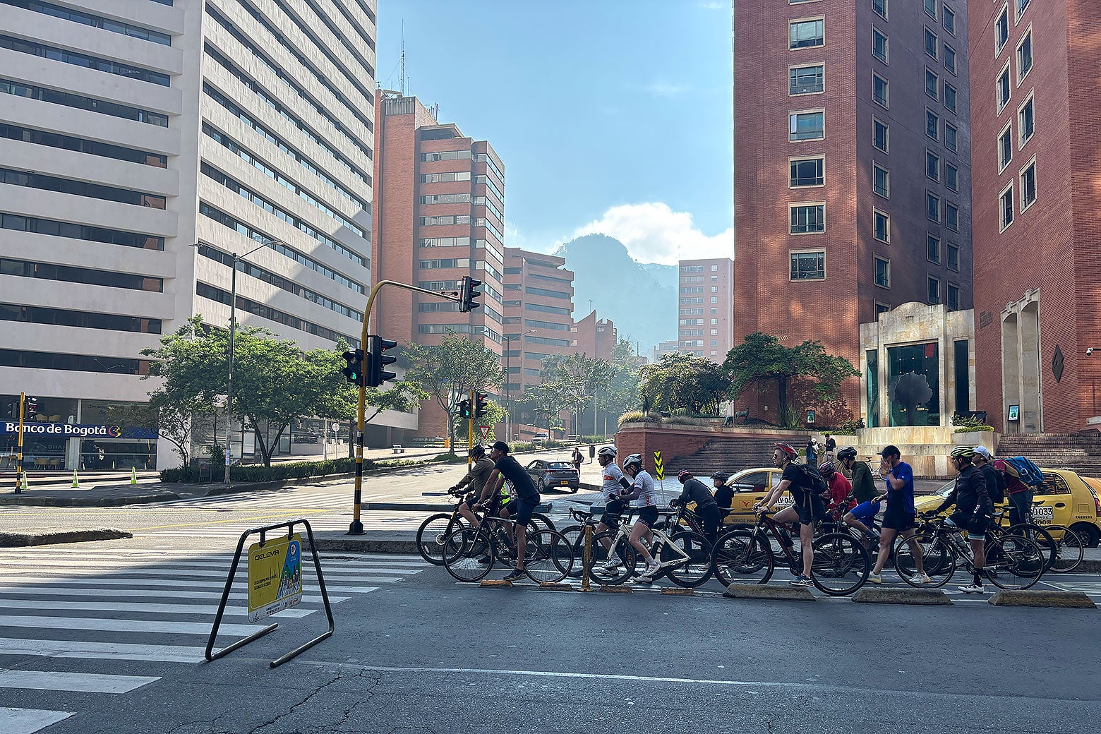 Mountains can be seen in the background of a blocked-off intersection with many bikers in it.