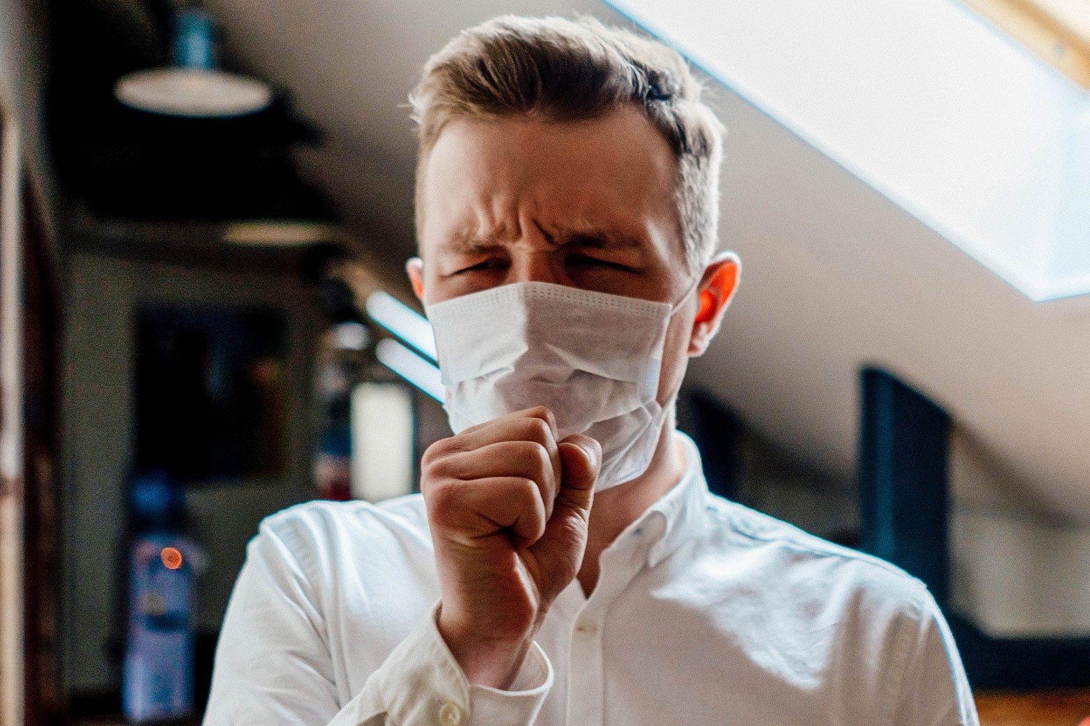Stock image of a man wearing a medical mask and coughing.