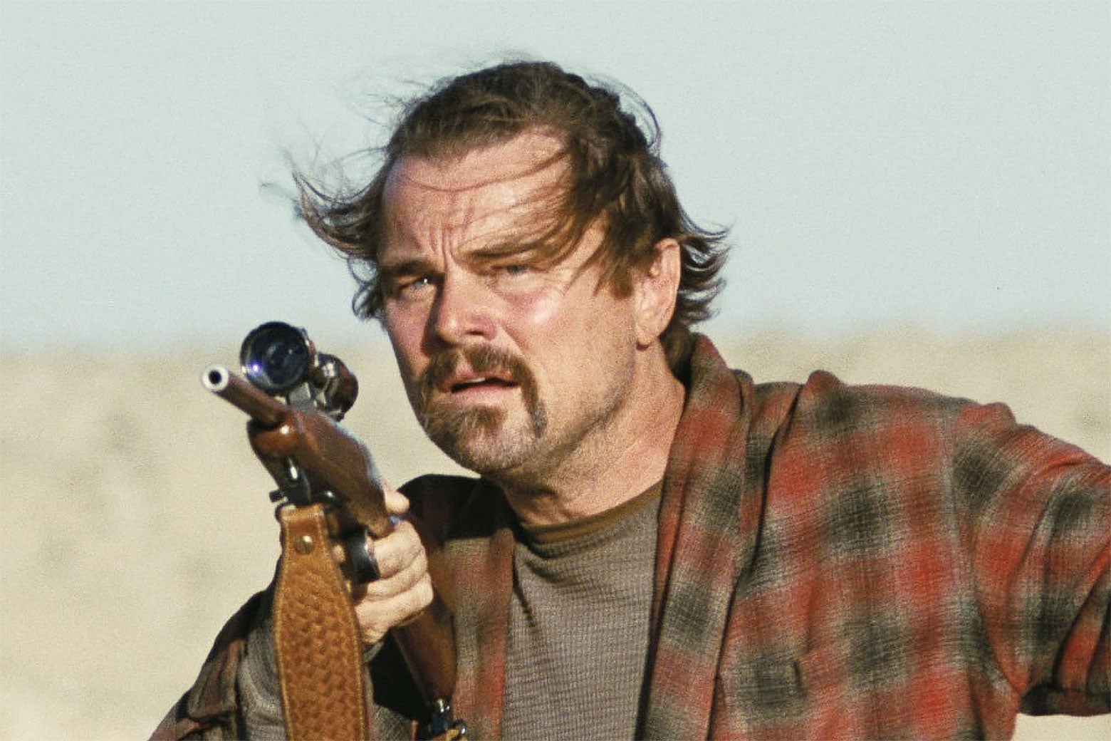Filmin bir sahnesinde Leonardo DiCaprio, Bob/Pat rolünde rüzgarlı bir tarlada tüfek tutuyor.
