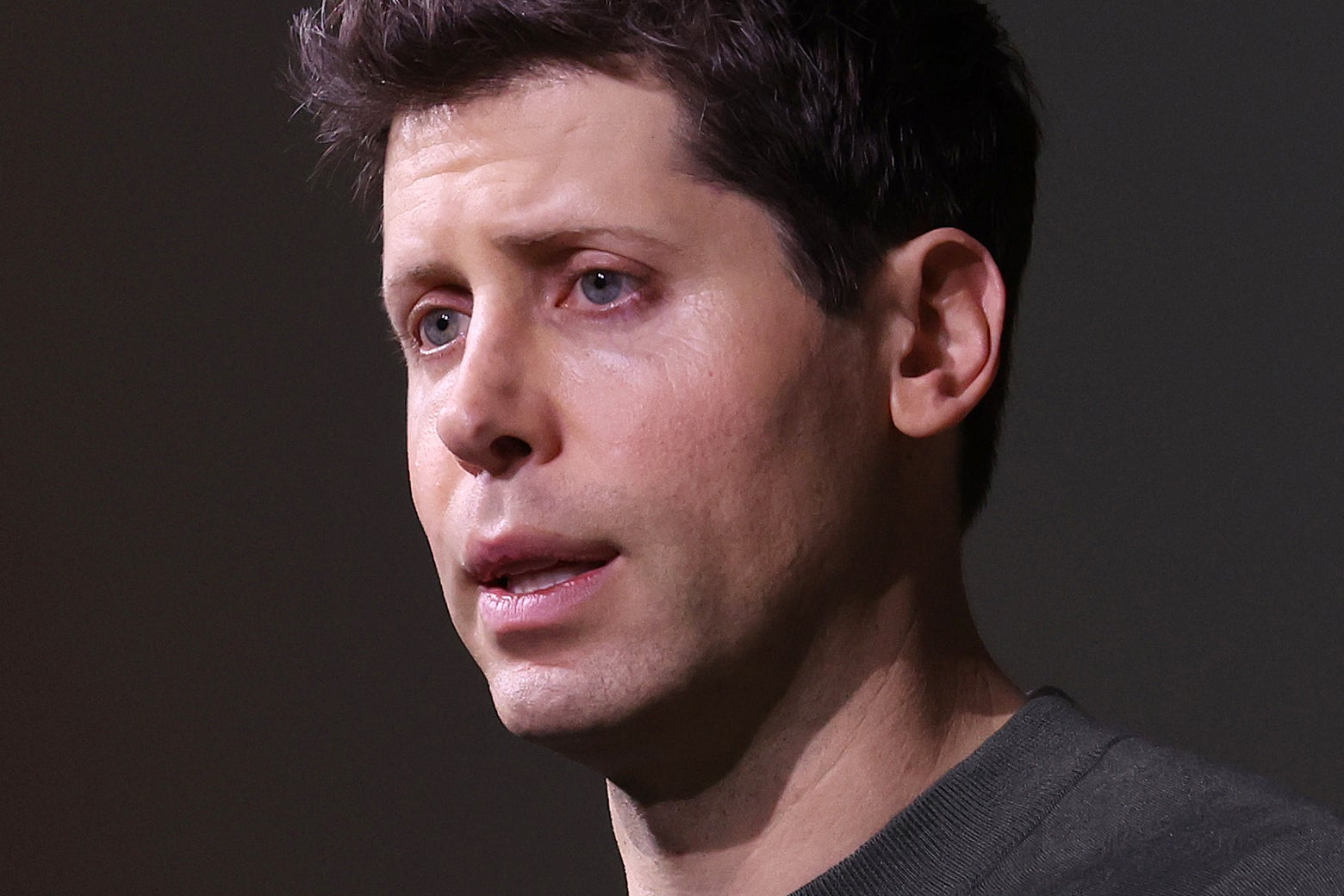 Sam Altman wears a black T-shirt and has his mouth open to speak. 