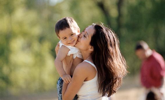 Mother holding and kissing her son outdoors.
