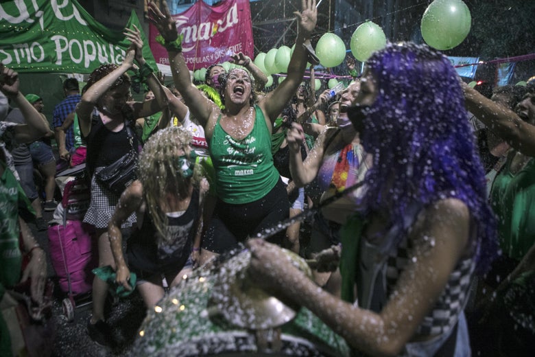 A crowd of mostly women dancing and shouting amid confetti, flags, and green balloons