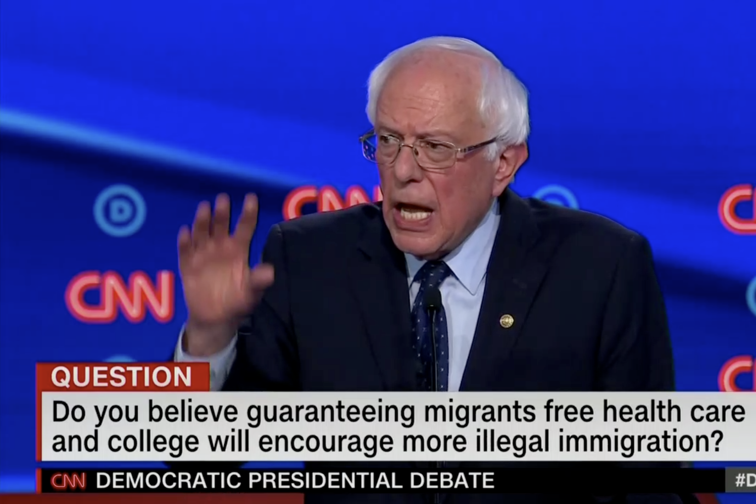 In this screengrab from CNN, Bernie Sanders debates. The banner reads: "Do you believe guaranteeing more migrants free health care and college will encourage more illegal immigration?"