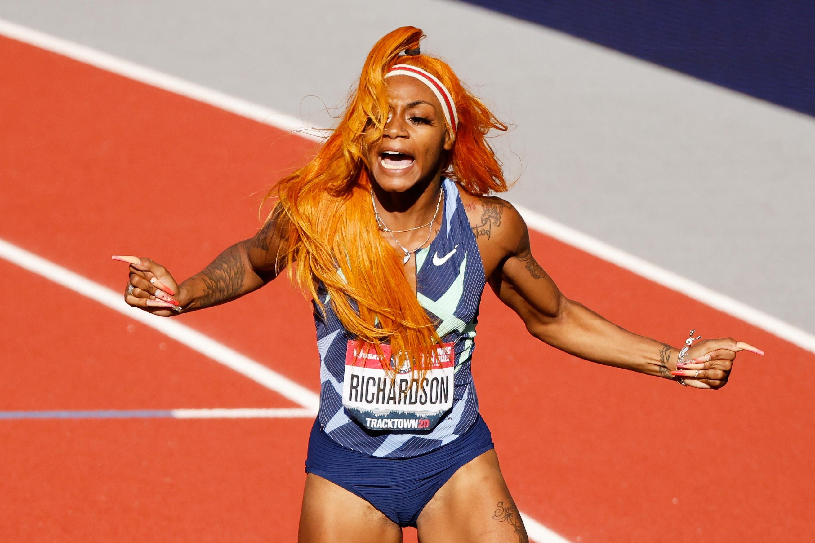 A woman with bright orange hair celebrates on a track.