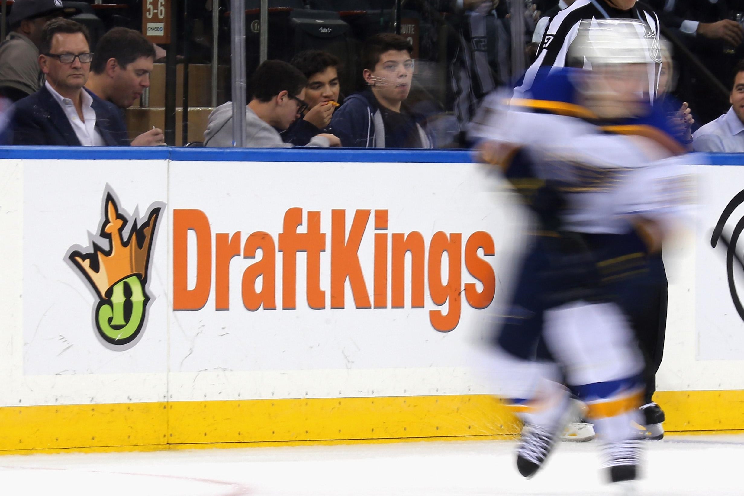 A blurry image of a hockey player skates in front of a dasher board advertising the betting website DraftKings at Madison Square Garden. 