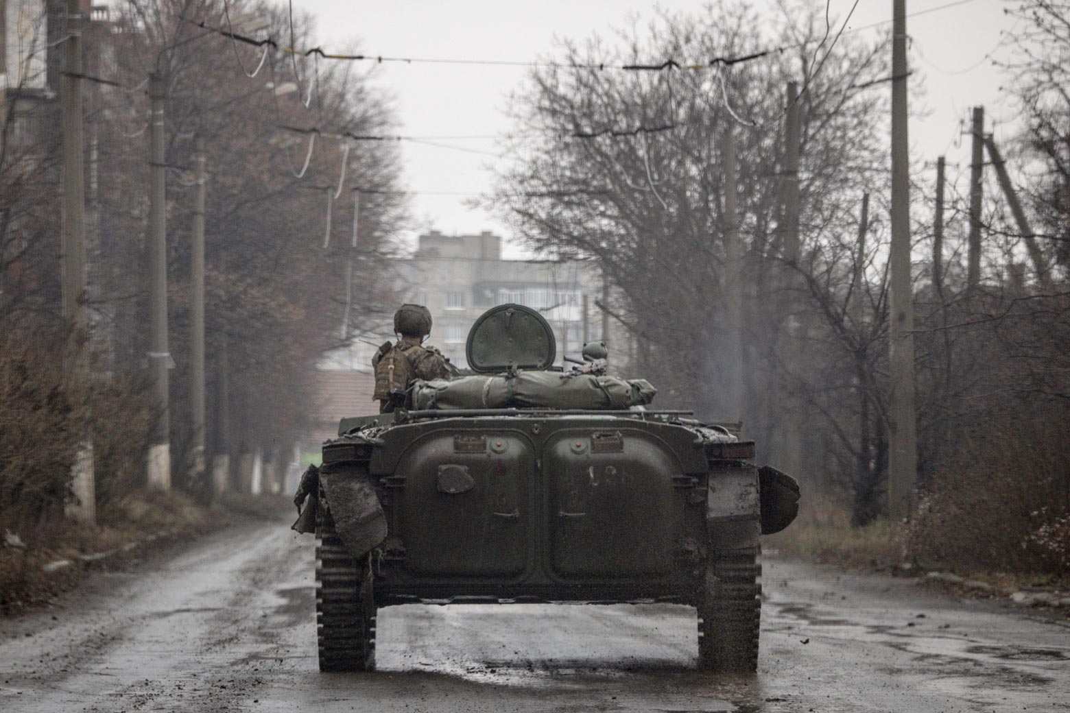 A soldier in an infantry fighting vehicle drives down a tree-lined street.