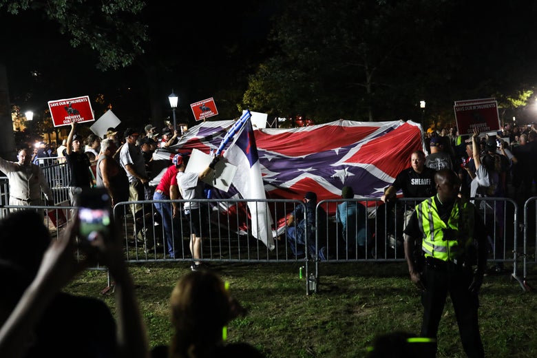 Pro-confederacy protestors hold up Christian Flags and Confederate flags inside a pen guarded by police.