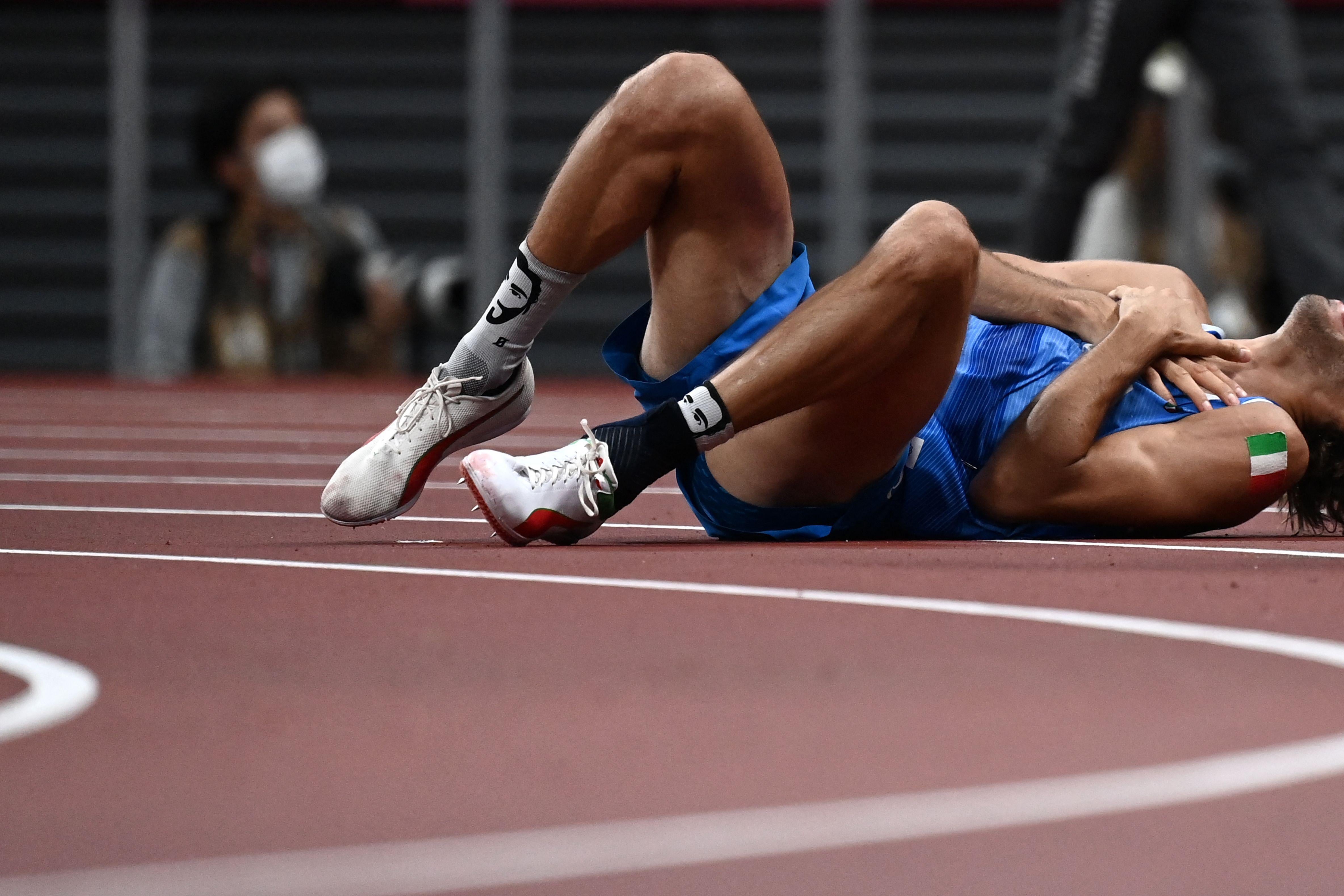 A high jumper lies on his back on the track, rolling on the ground, holding his hands to his heart, and screaming.
