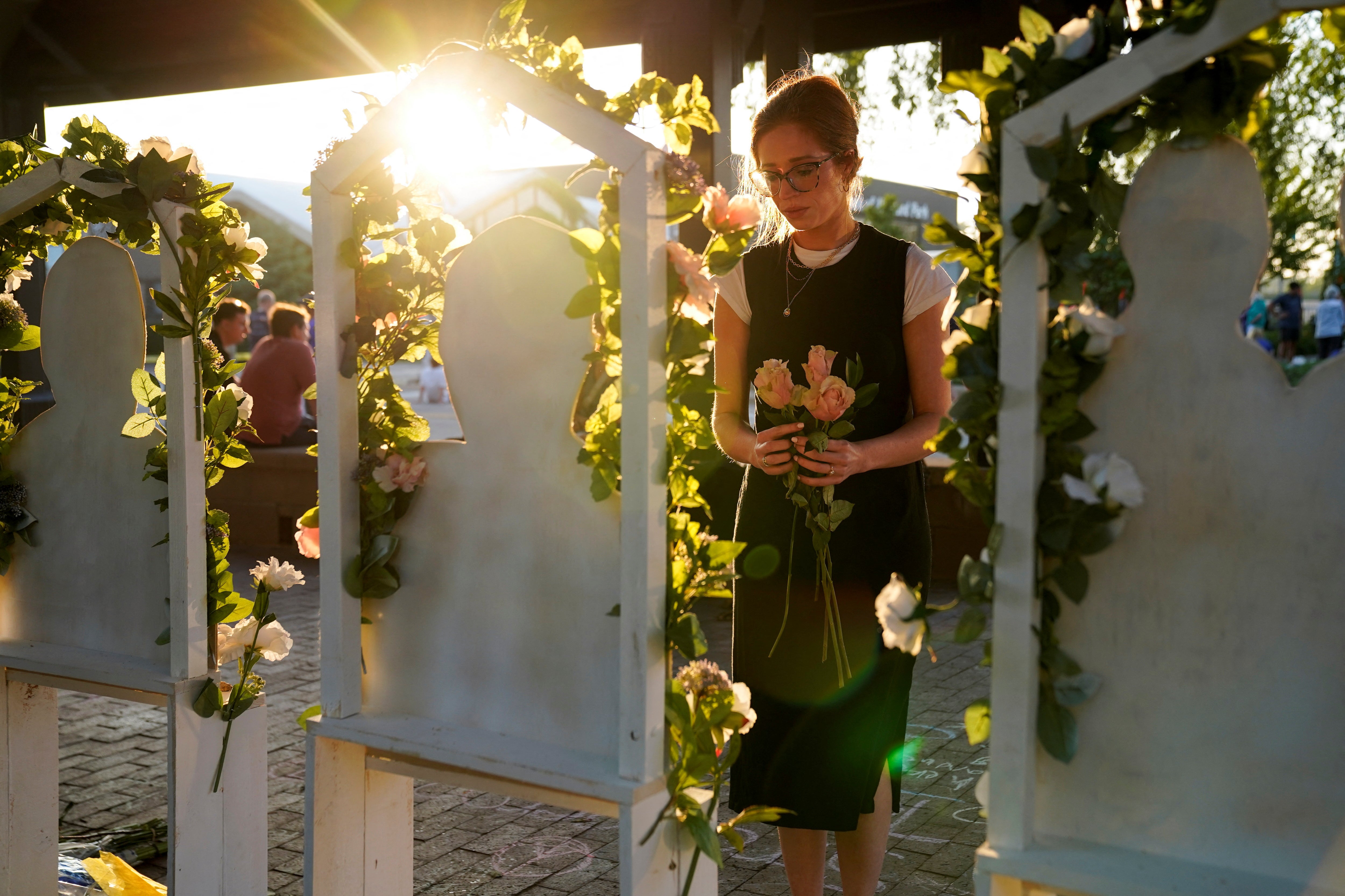 A mourner visits a memorial for victims—she holds roses that she is placing in front of the cardboard cut outs of each victim.