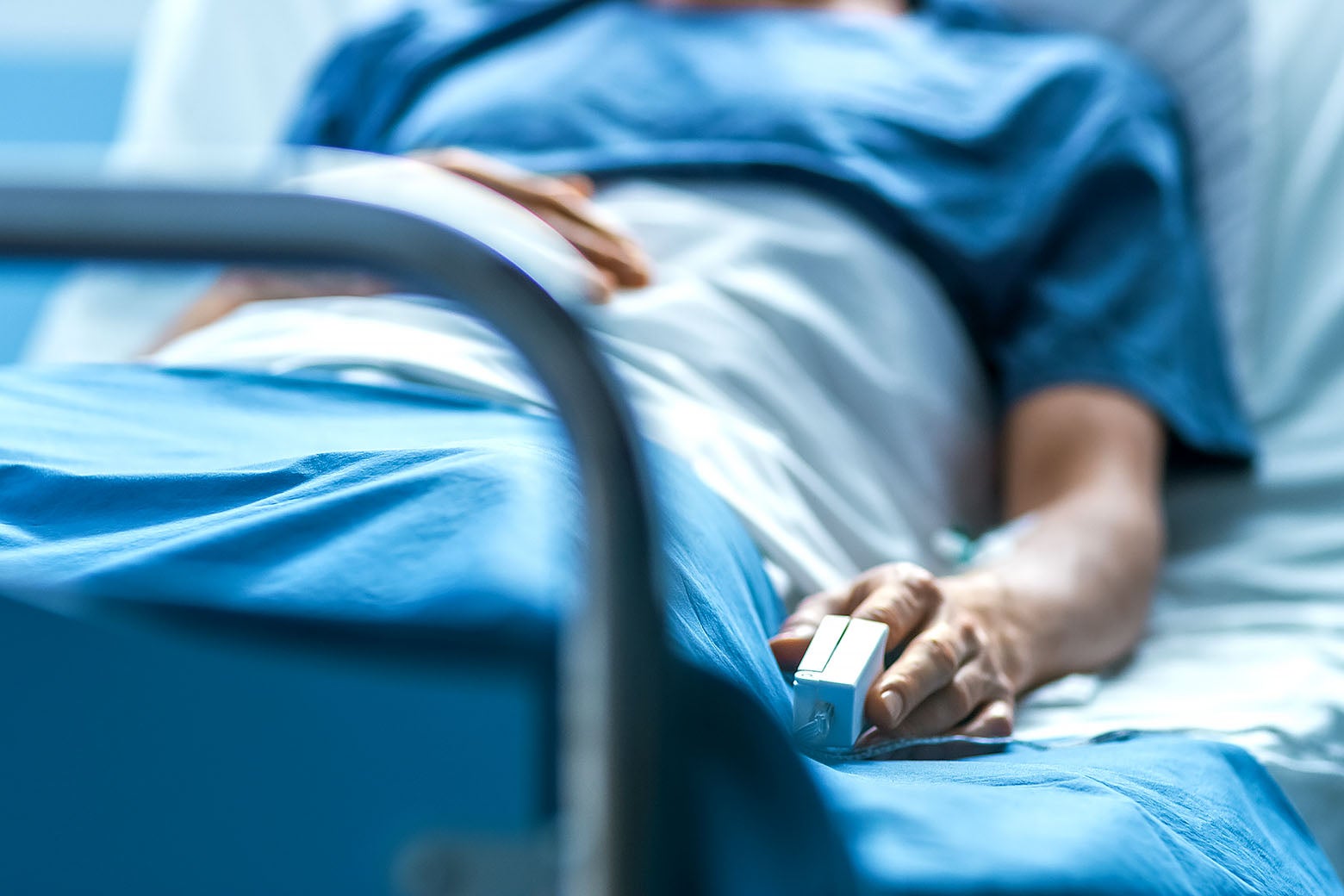 A man lying in a hospital bed with a heart monitor cord attached to his left index finger.