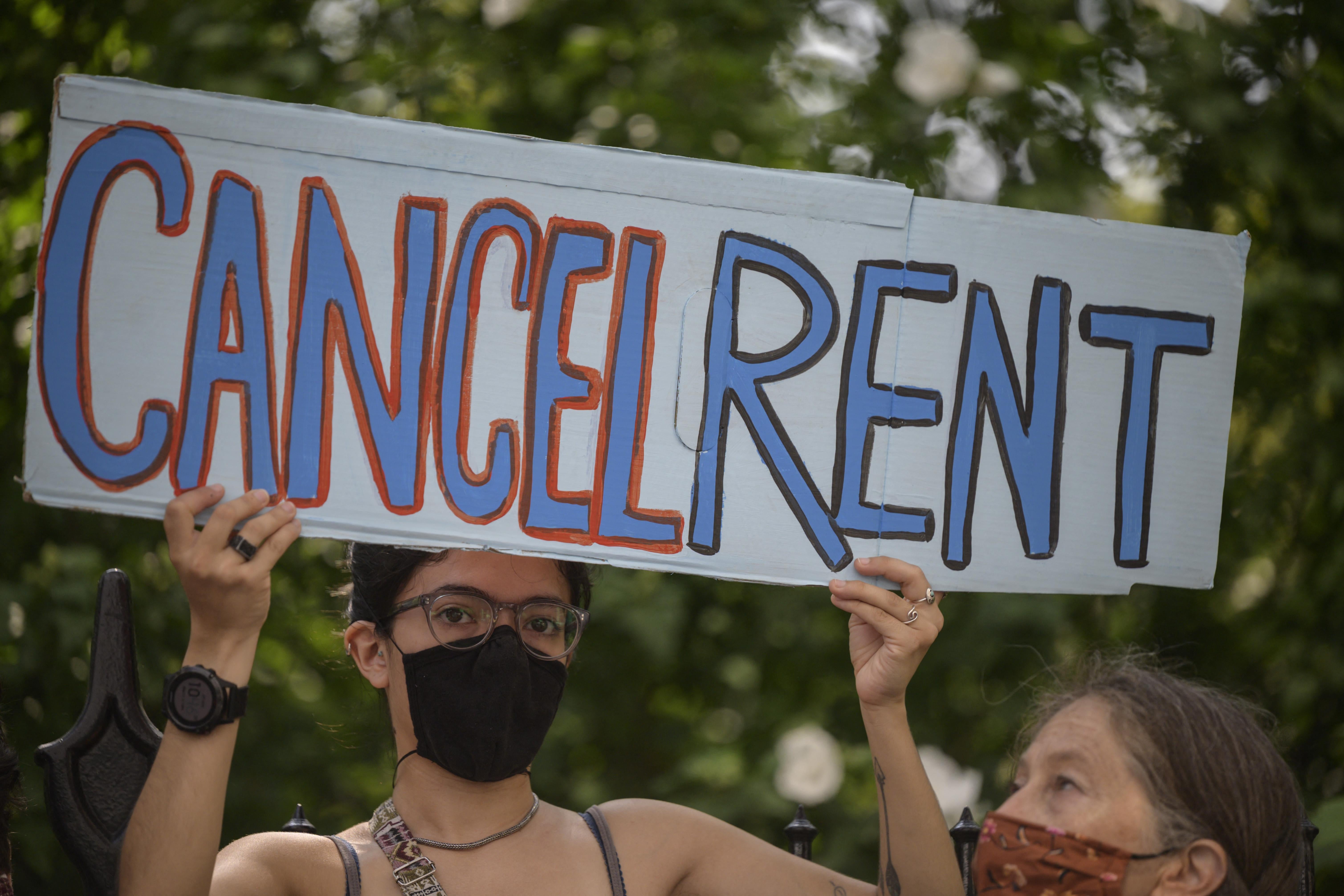A masked demonstrator holds up a handmade sign that reads: Cancel rent.