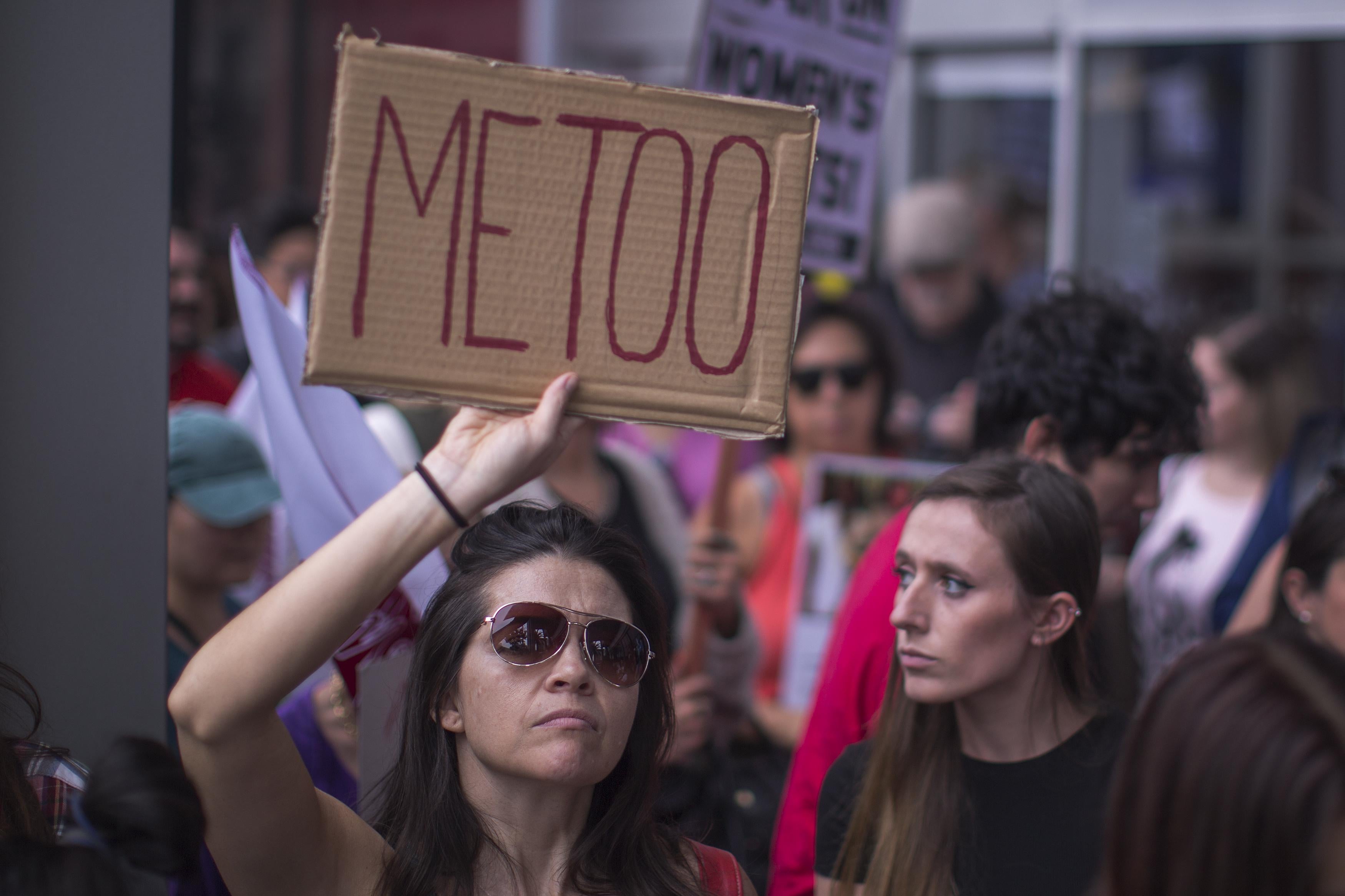 A woman holds up a cardboard sign that says "METOO."