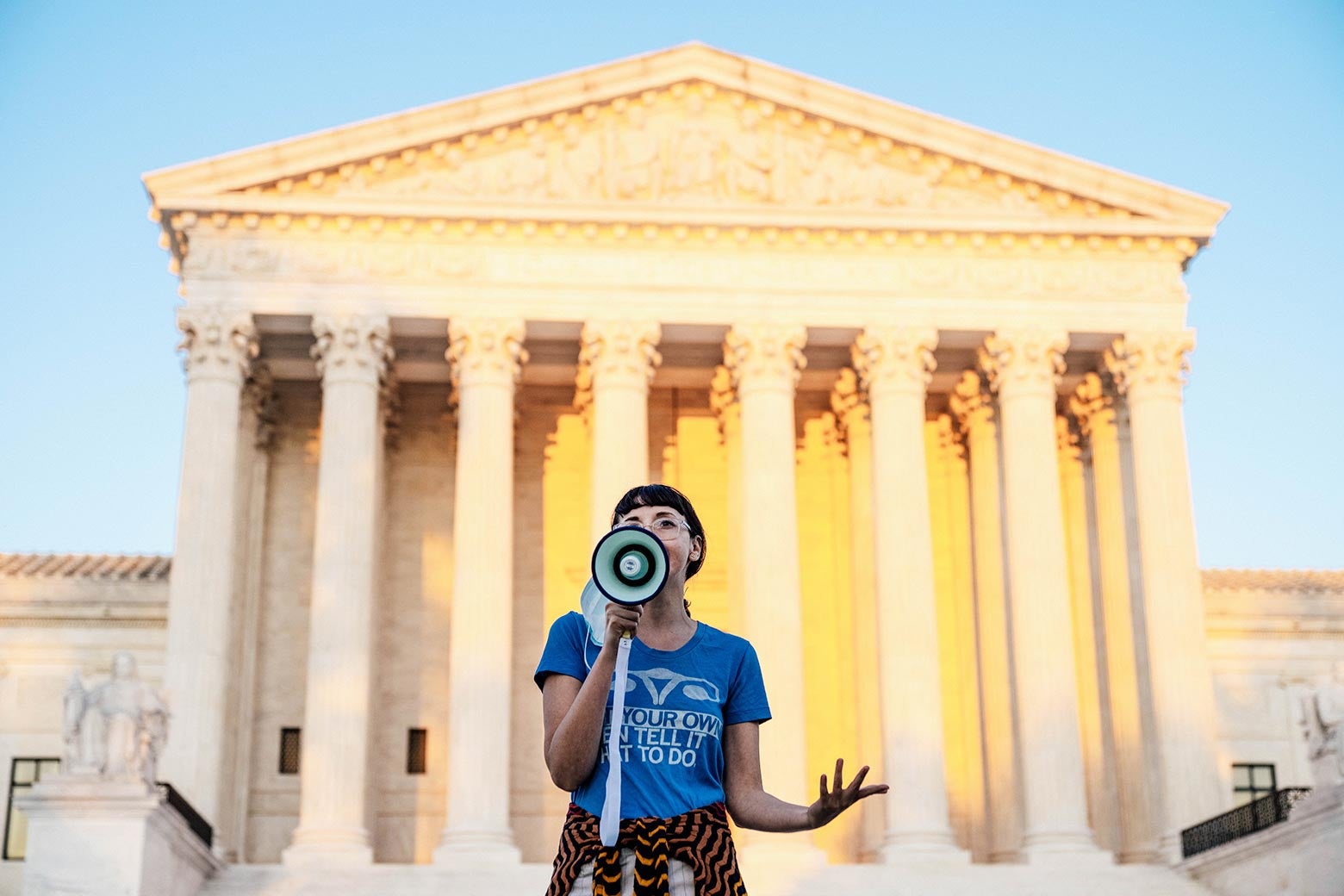 A protester speaks through a megaphone against a majestic view of the Supreme Court.