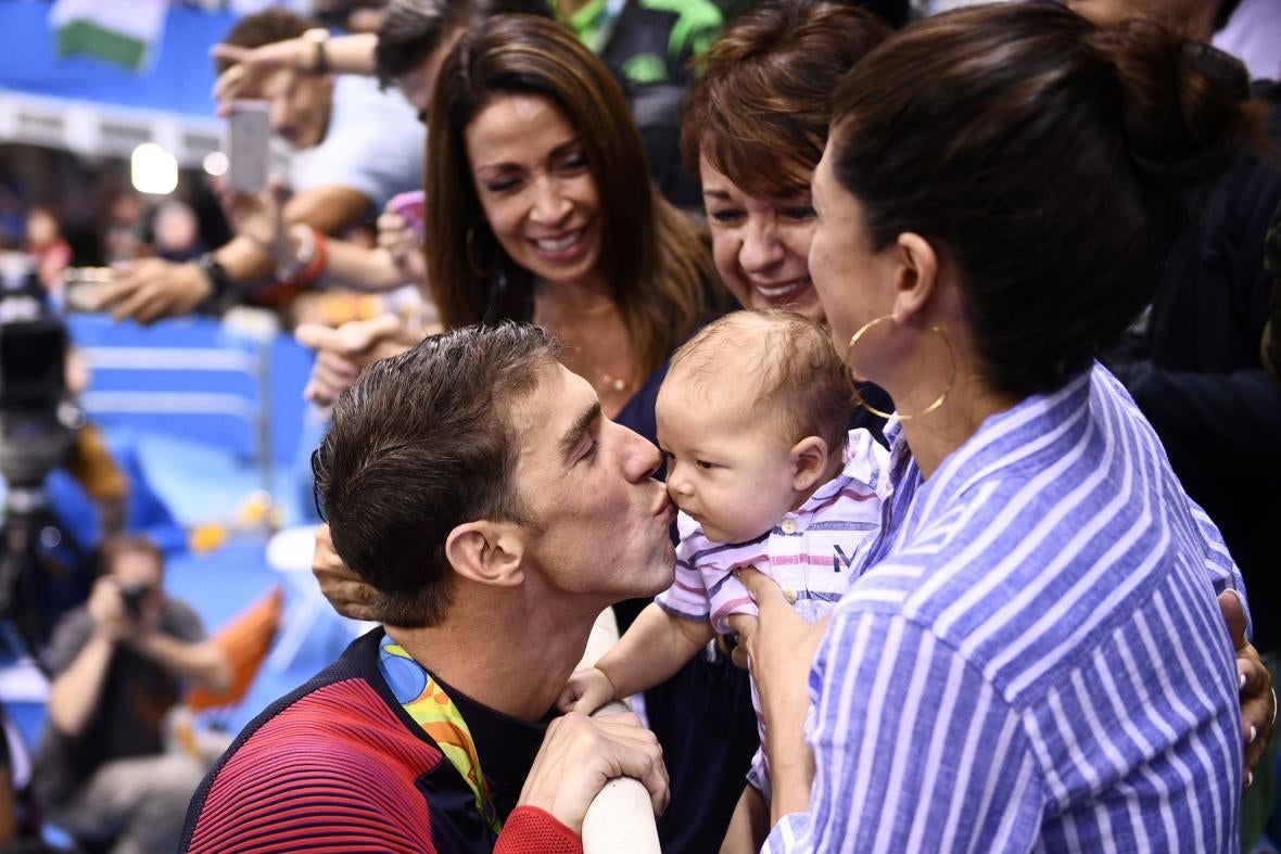 Phelps kisses Boomer in the stands, with his wife, mother, and a third woman around them and smiling