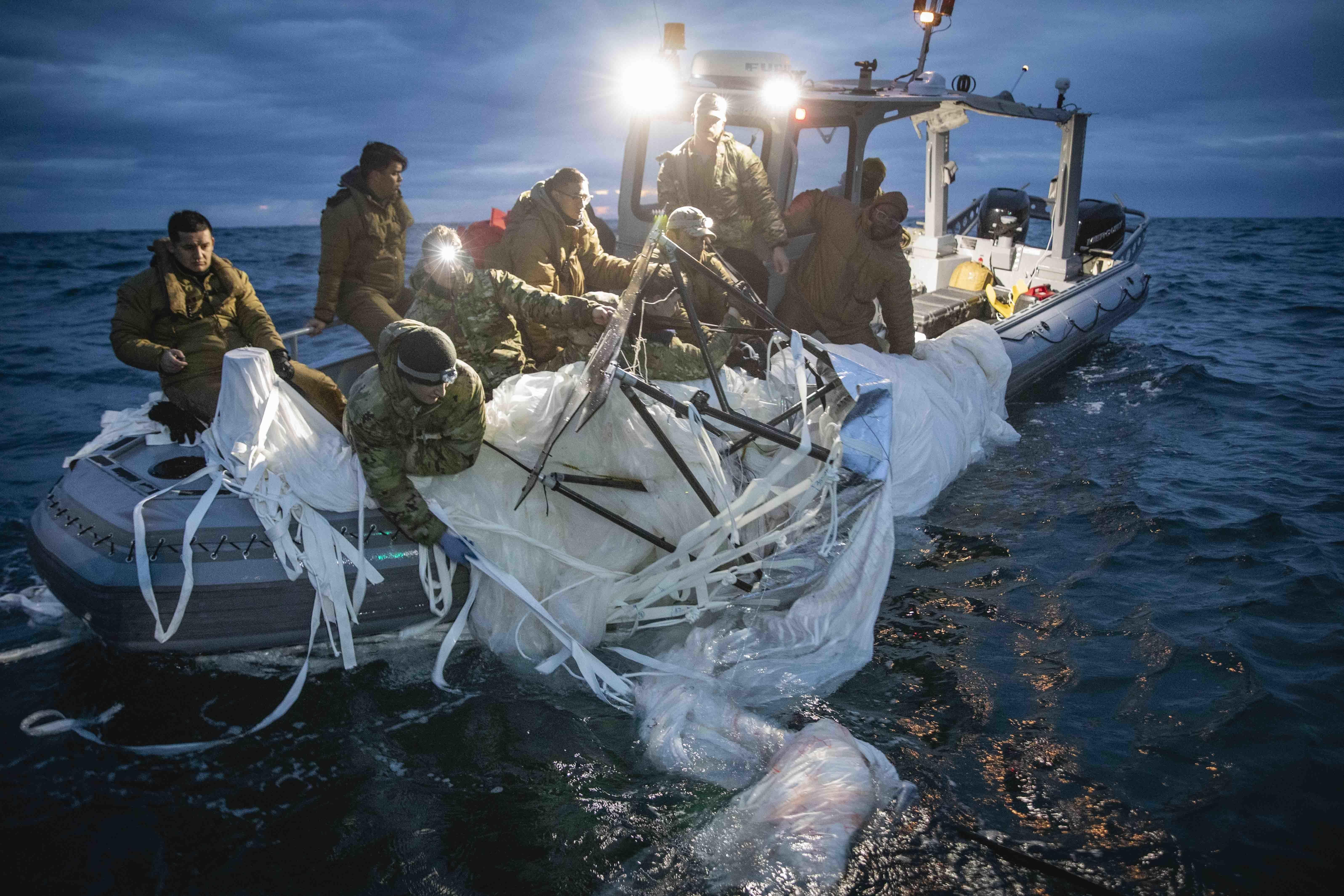 A large white section of balloon debris being hauled into a boat by several sailors.