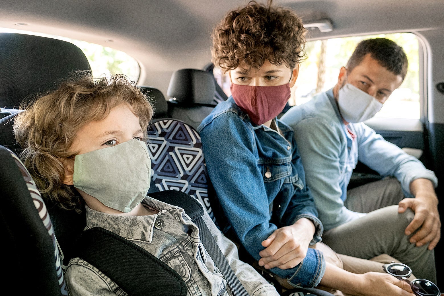Masked kids in the back seat of a car.