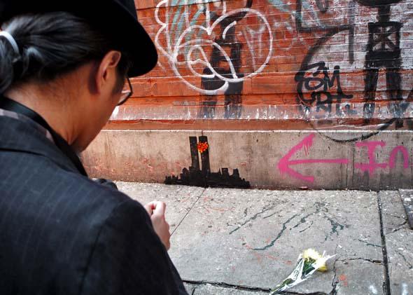 A man photographs Banksy's latest work depicting the New York City skyline with the former World Trade Center Twin Towers October 15, 2013 in the Tribeca neighborhood of New York City. 