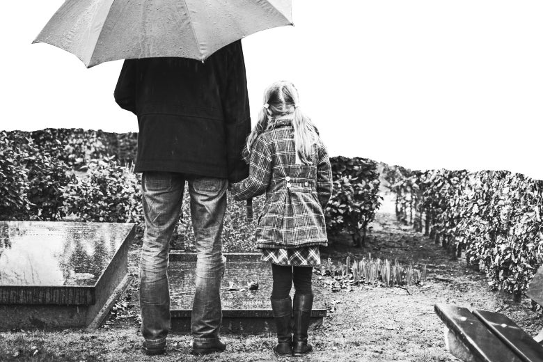 A father and daughter stand over a grave in the rain.