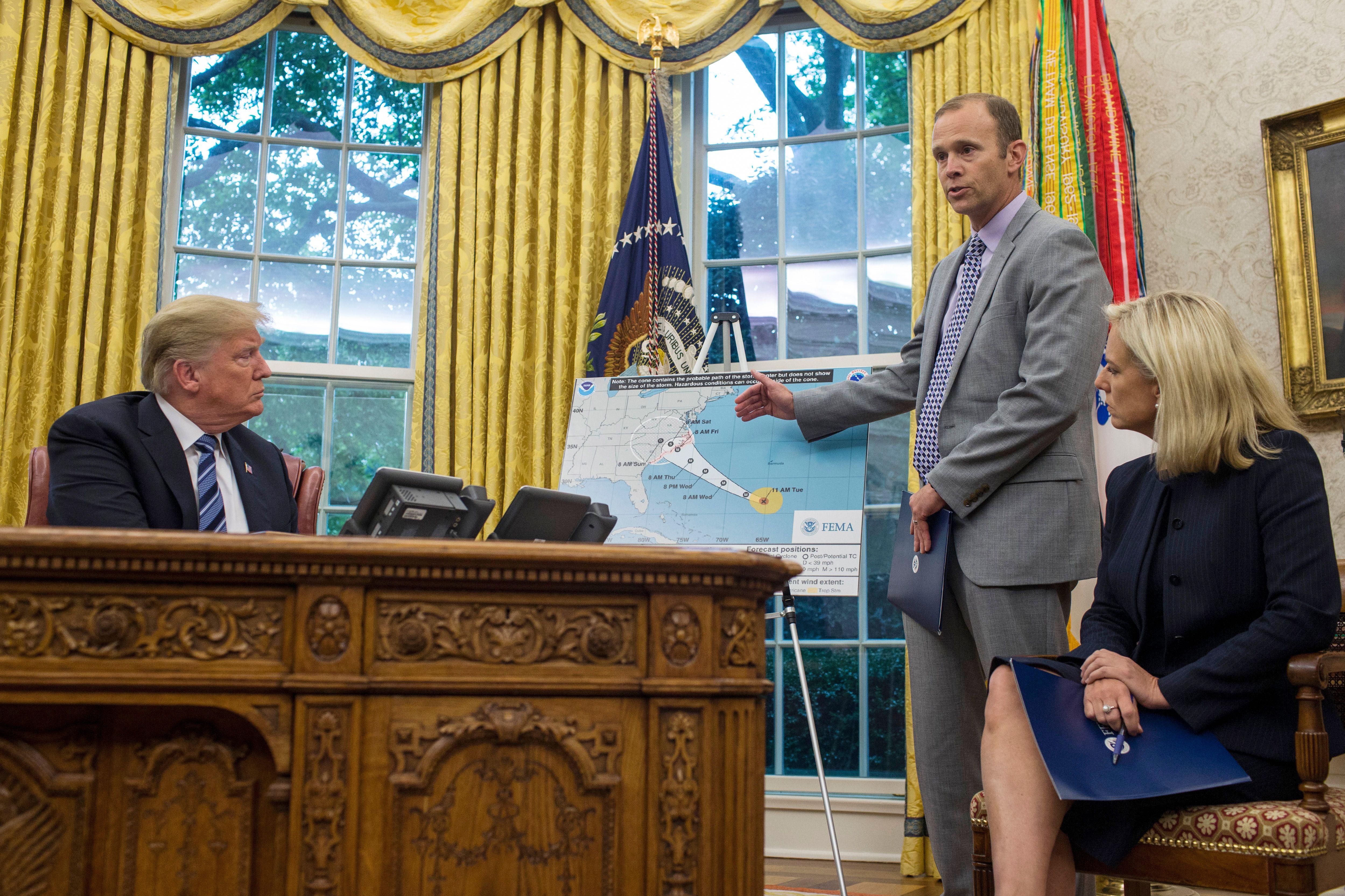 Donald Trump sits at his desk in the Oval Office while FEMA Administrator Brock Long stands and points to a map of Hurricane Florence's path, next to U.S. Secretary of Homeland Security Kirstjen Nielsen.