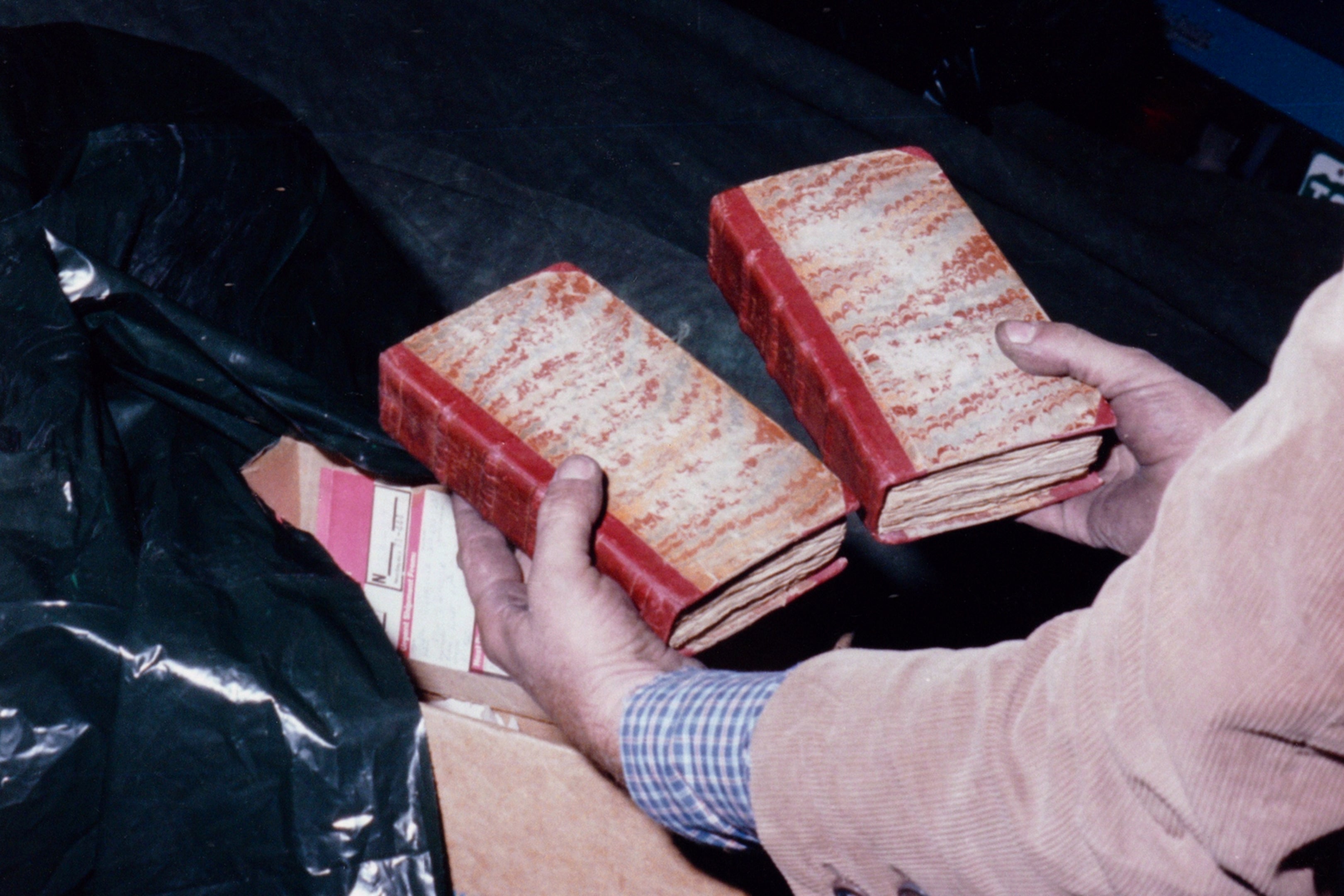 A man holds two ancient-looking books.