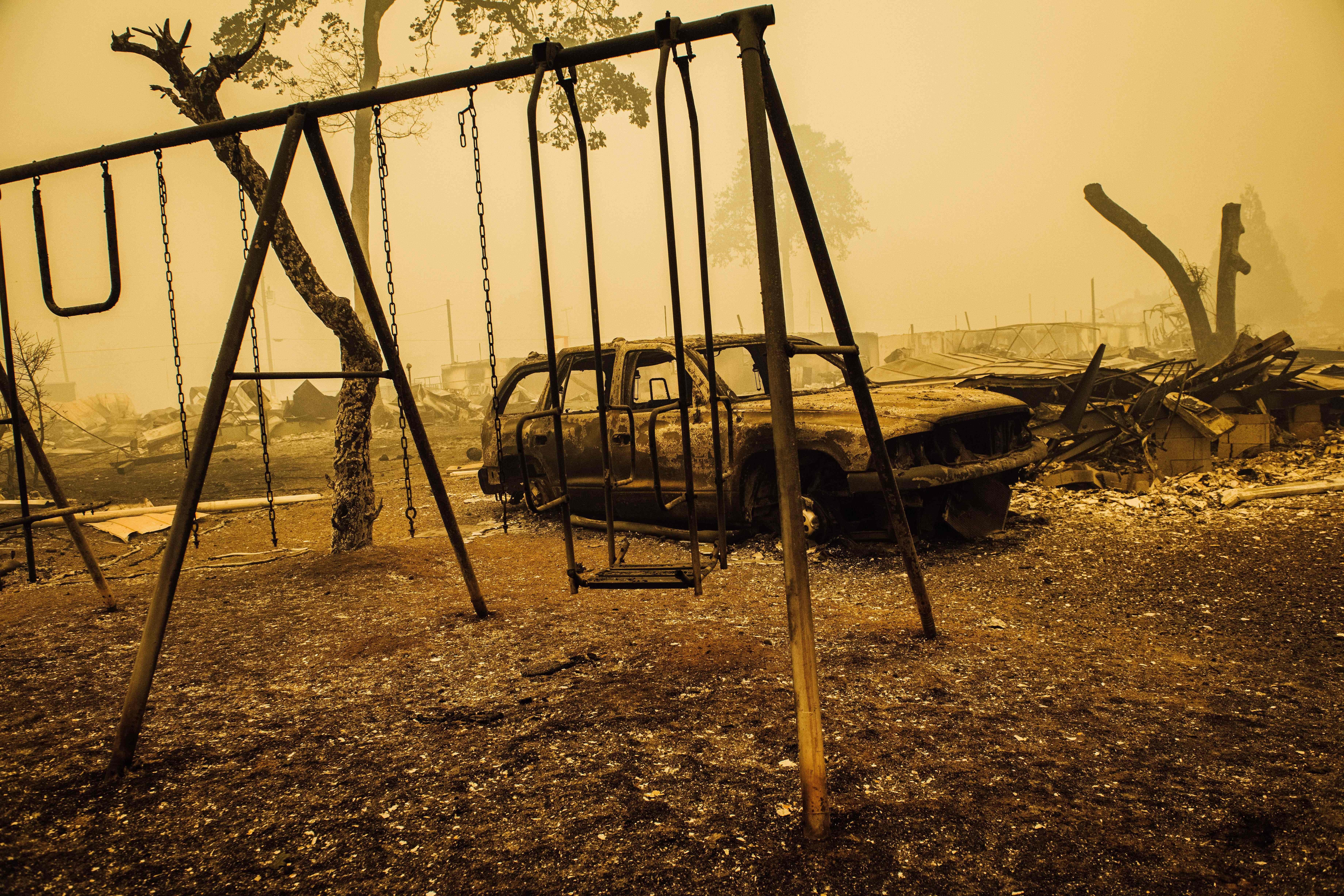 A charred car and swing set in a burned-out landscape yellow with smoke.