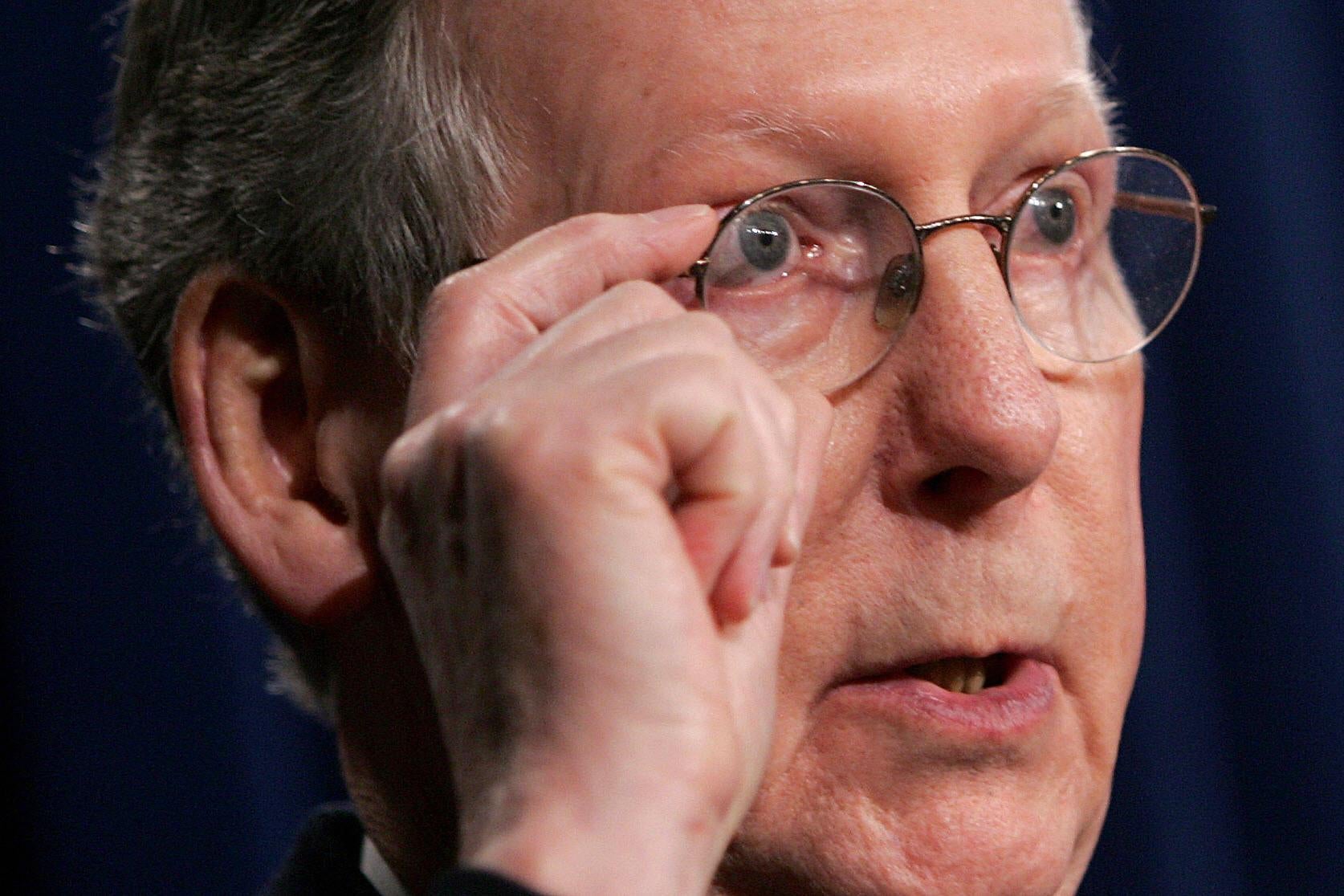 A close-up of Mitch McConnell's face, in which he puts his hand to his glasses