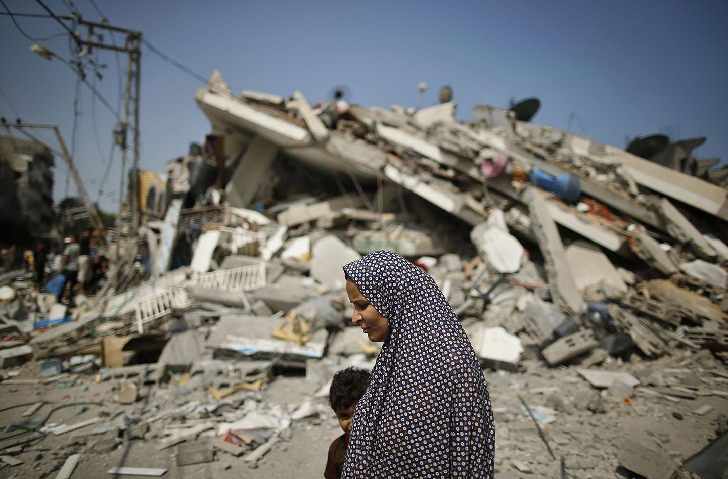 A Palestinian woman walks past the rubble of a residential building.