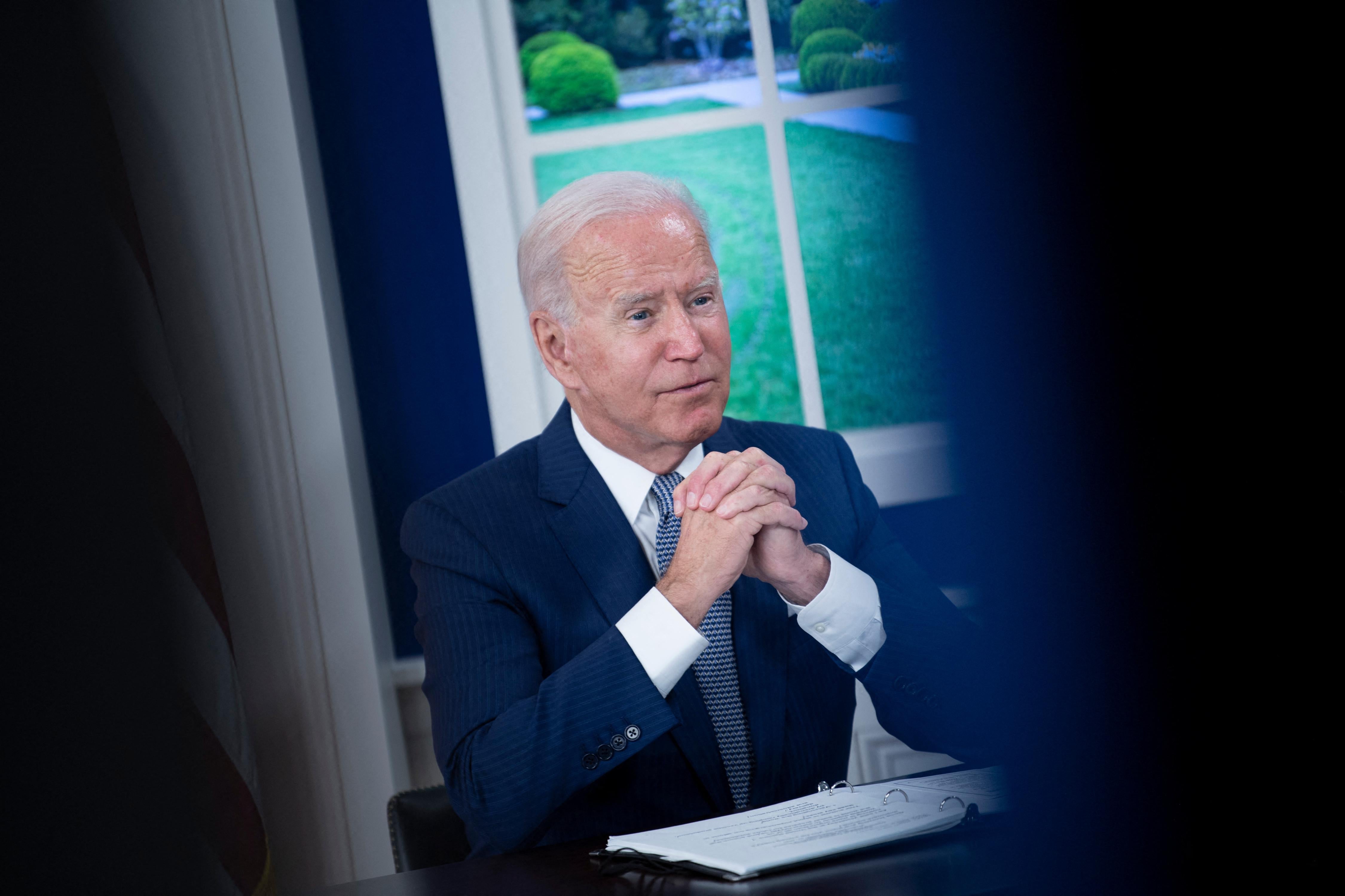 Joe Biden sits at a desk with hands near his chin.