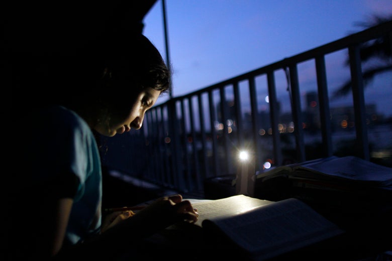 A Puerto Rican girl does her daily homework in her apartment balcony lit by a cellphone light.