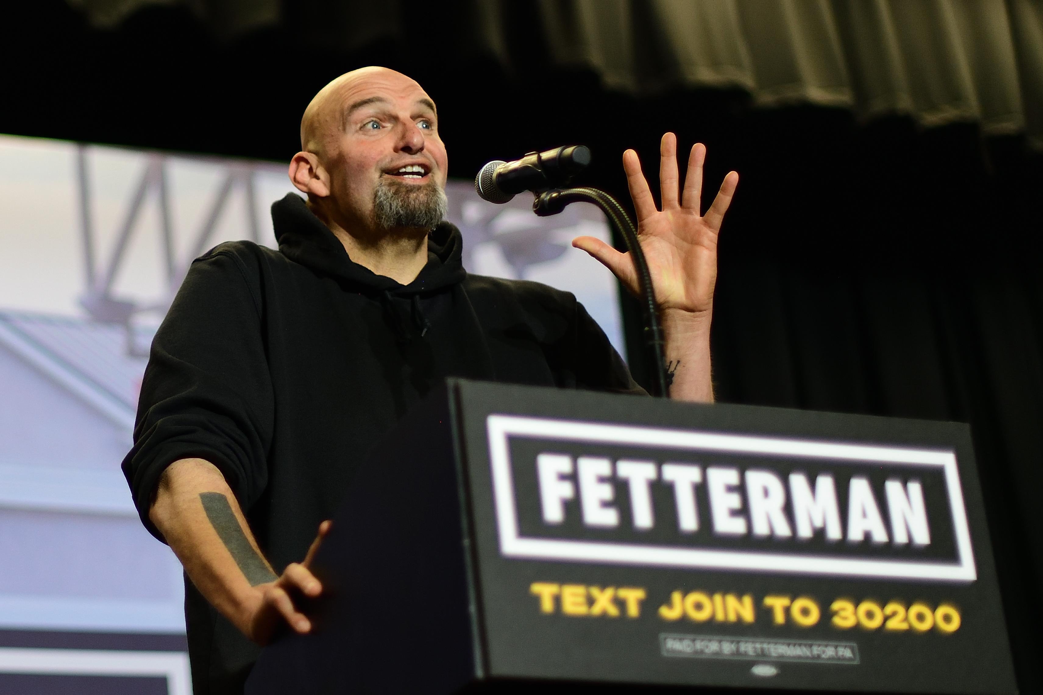 Democratic candidate for U.S. Senate John Fetterman stands at a podium while speaking at a rally.