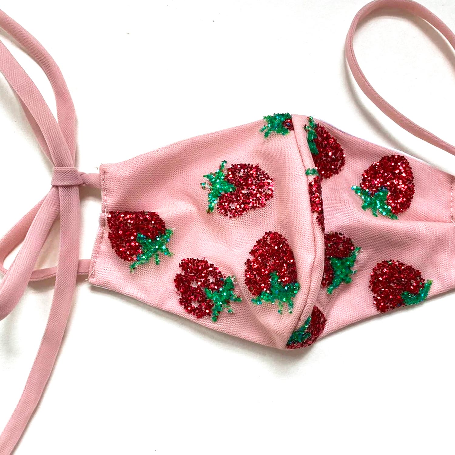 A pink mask with a strawberry sequin design lays against a white background