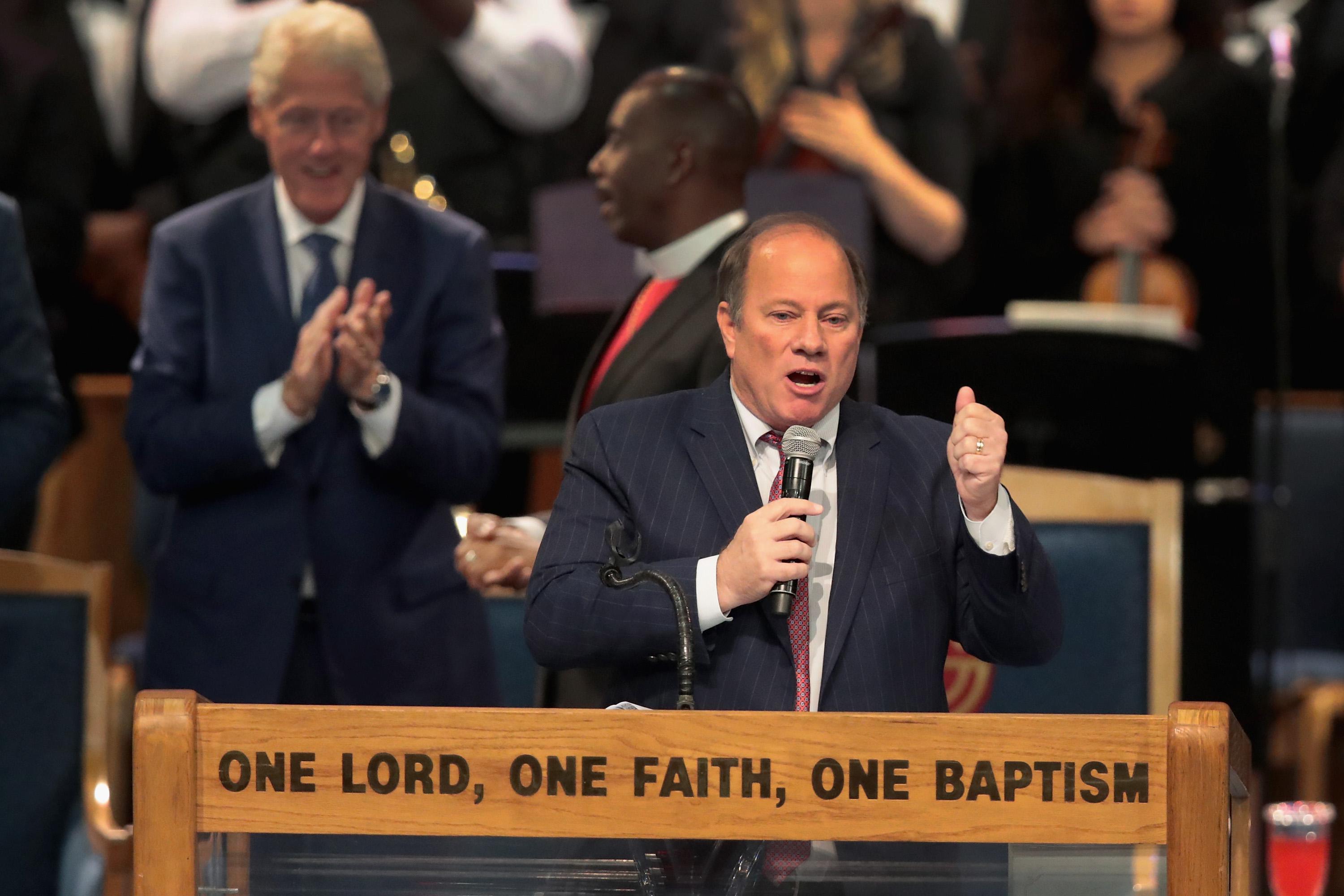 Mike Duggan stands on a pulpit with the words "One Lord, One Faith, One Baptism" on it.