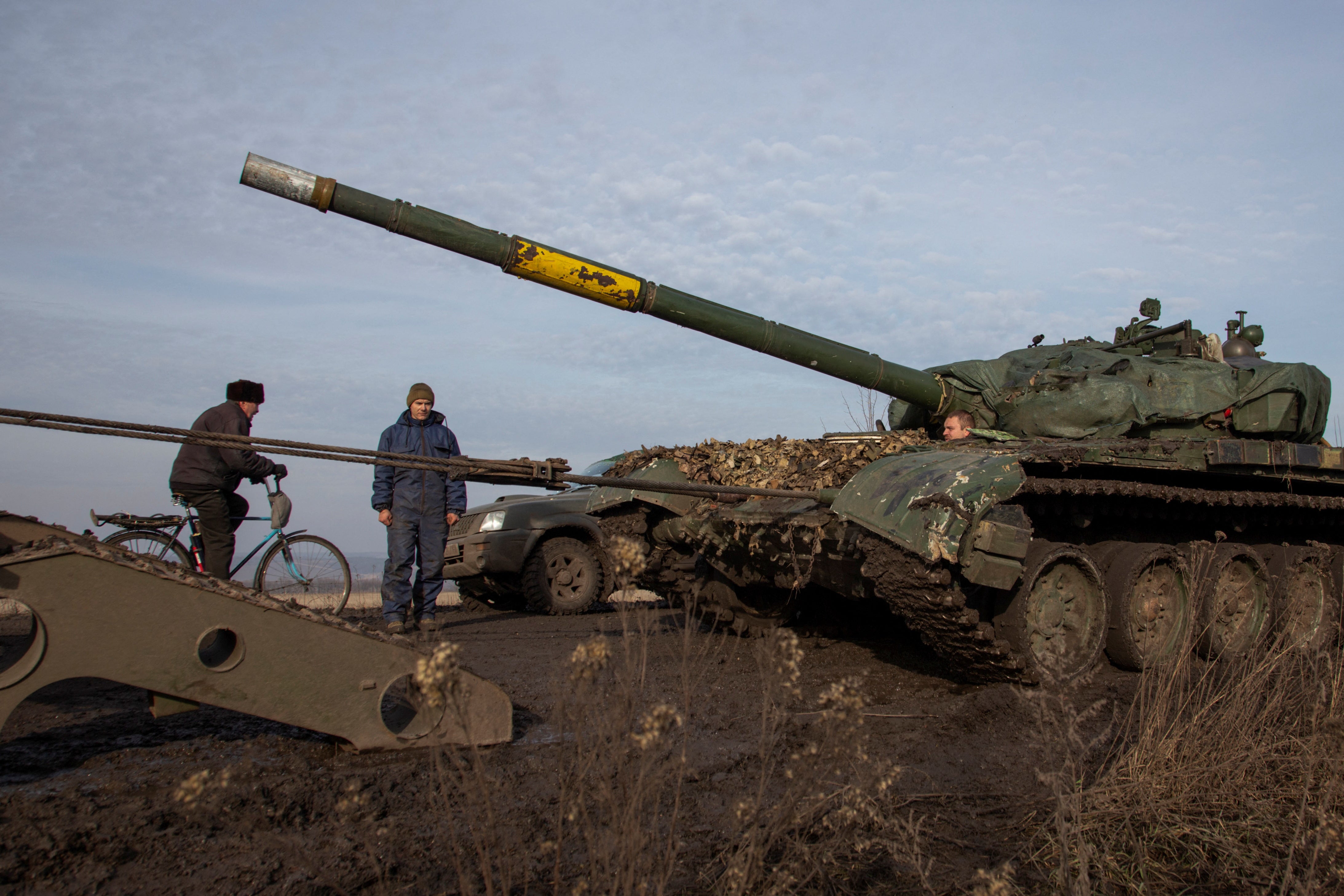 A photo of a tank, and a Ukrainian serviceman, and a man on a bike, in Ukraine.