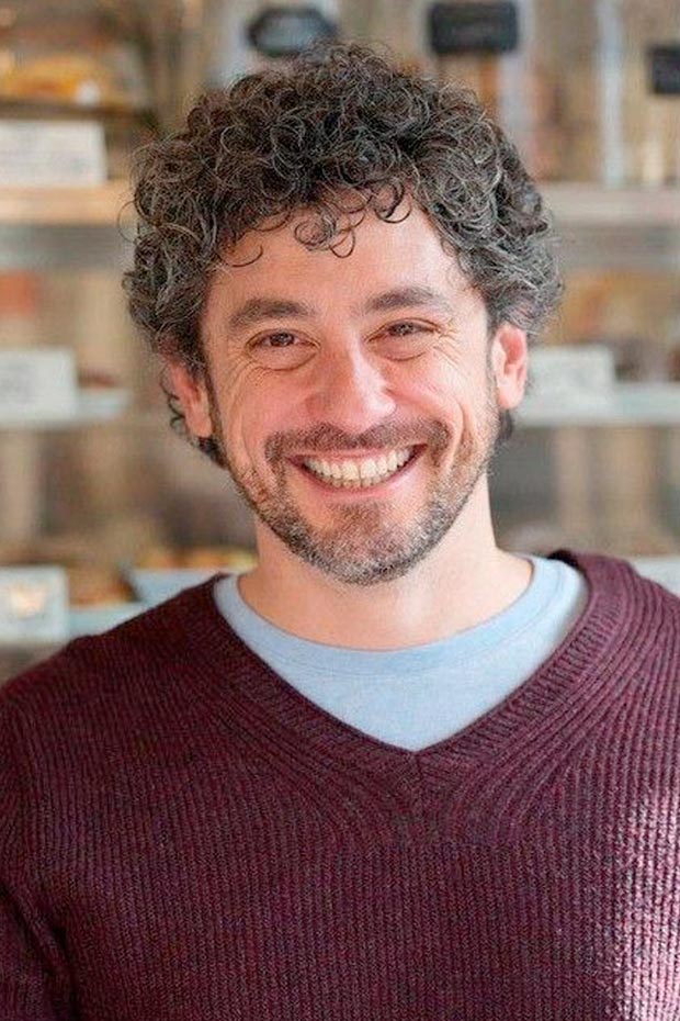 A man with curly hair smiles at the camera.