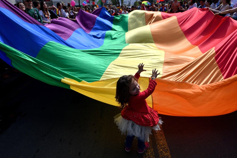 A child helps to wave a huge rainbow flag during the Gay Pride parade in the middle of the street.
