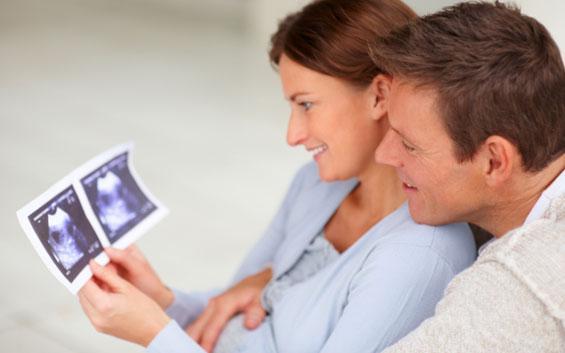 Happy parents couple holding a sonogram of their unborn child