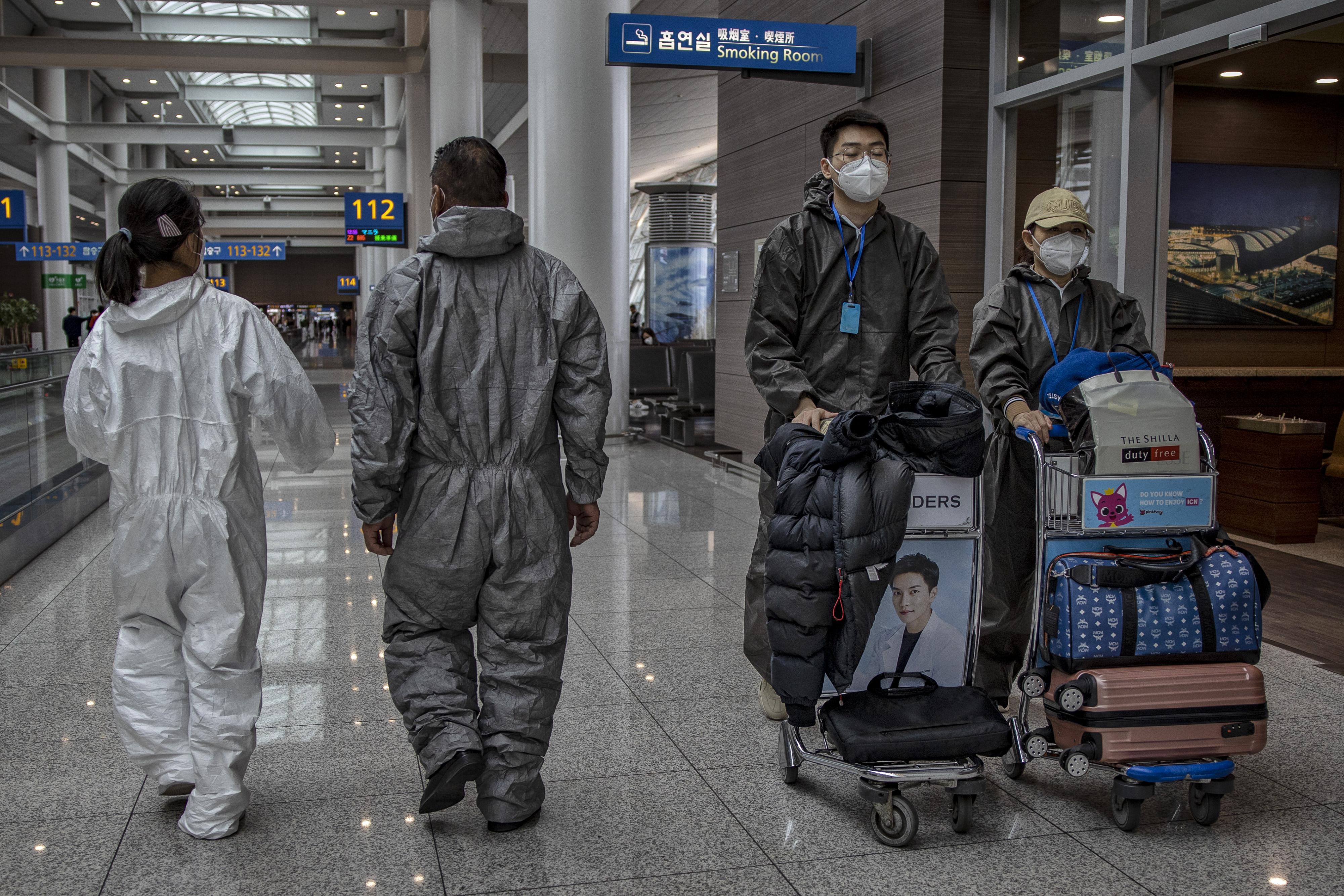 People wearing protective suits and face masks walk in the airport