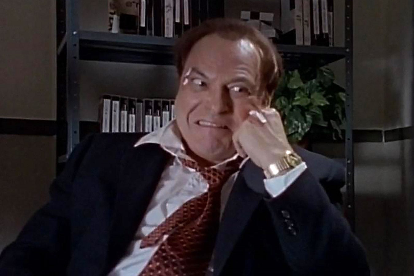 Rip Torn, in a suit and tie, grimaces and rests his head on his hand.