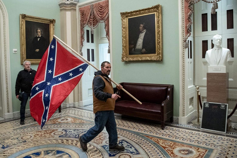 A man walks through the Capitol carrying a Confederate battle flag over his shoulder