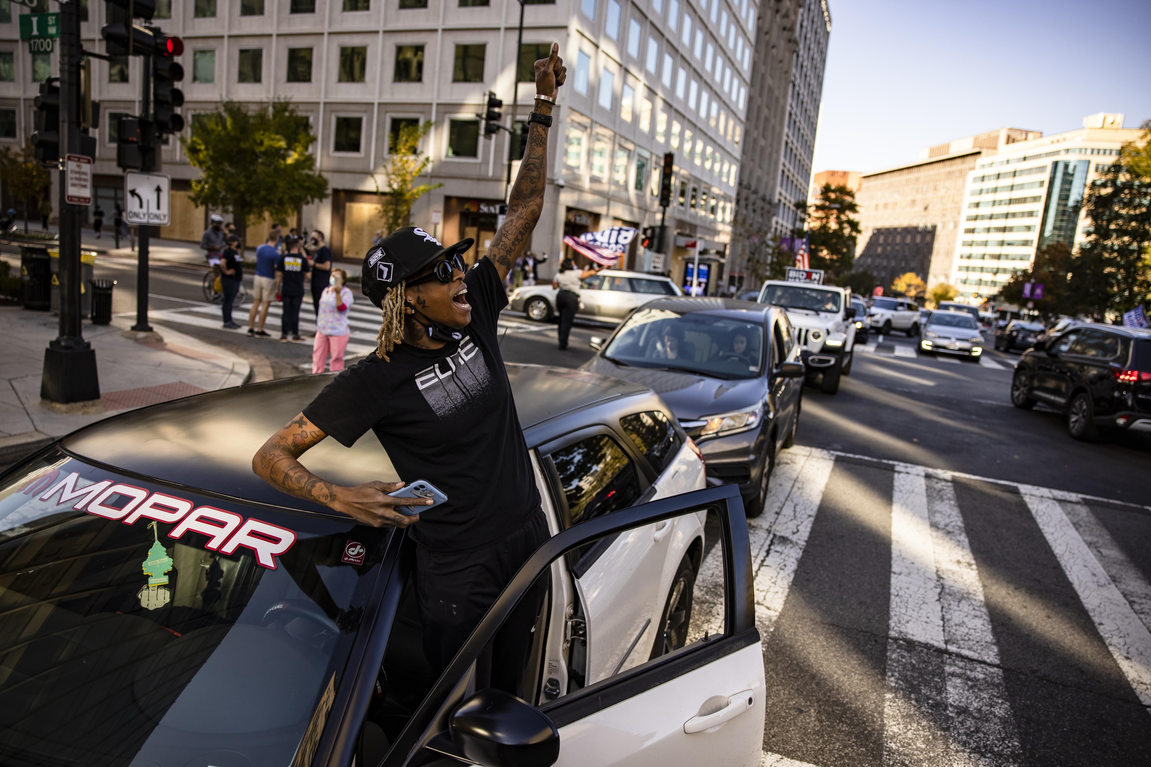 A person standing just out of their car raises their fist into the air in downtown Washington, DC.