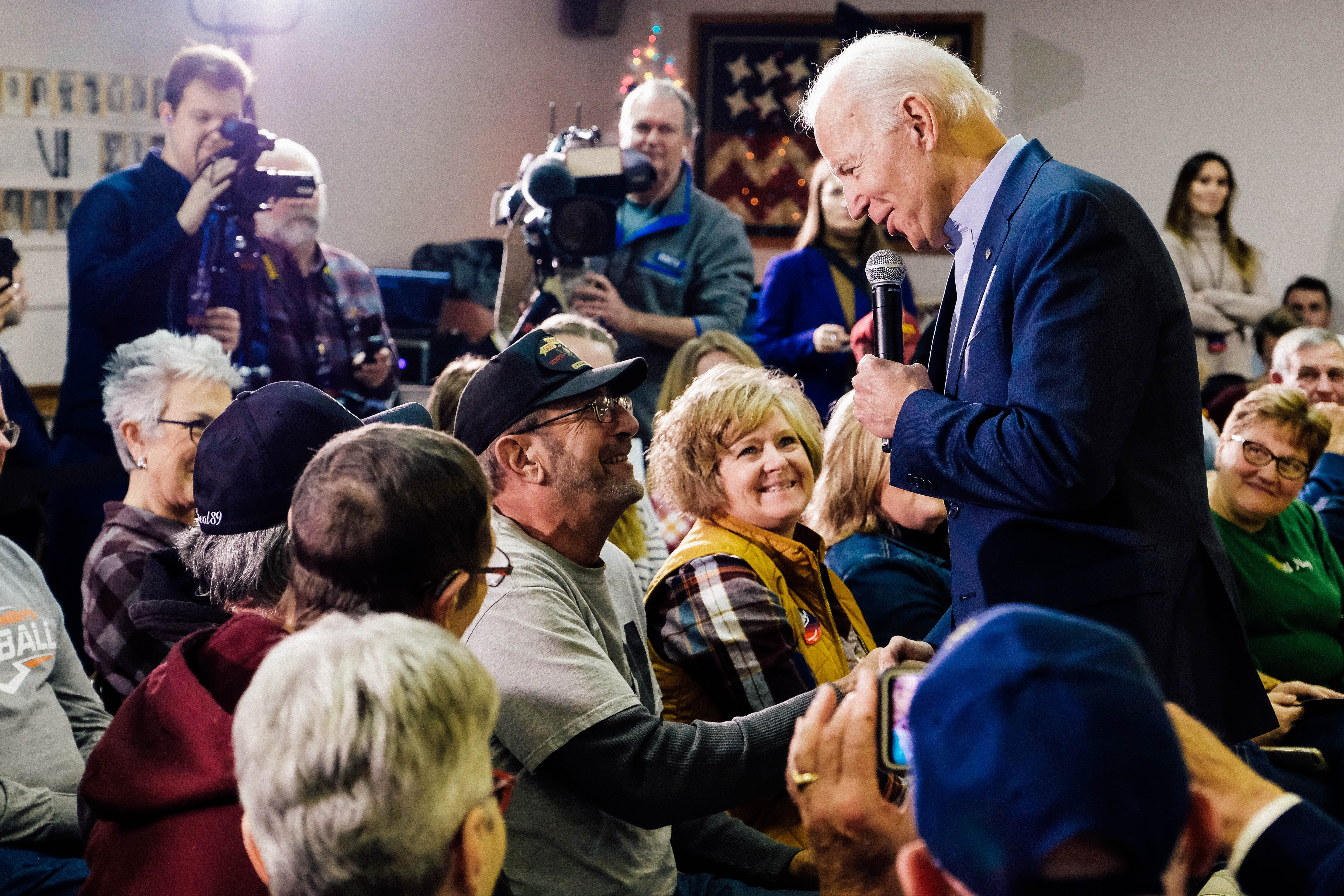 Biden, standing, shakes the hand of a man seated in the audience of a town hall–style event.