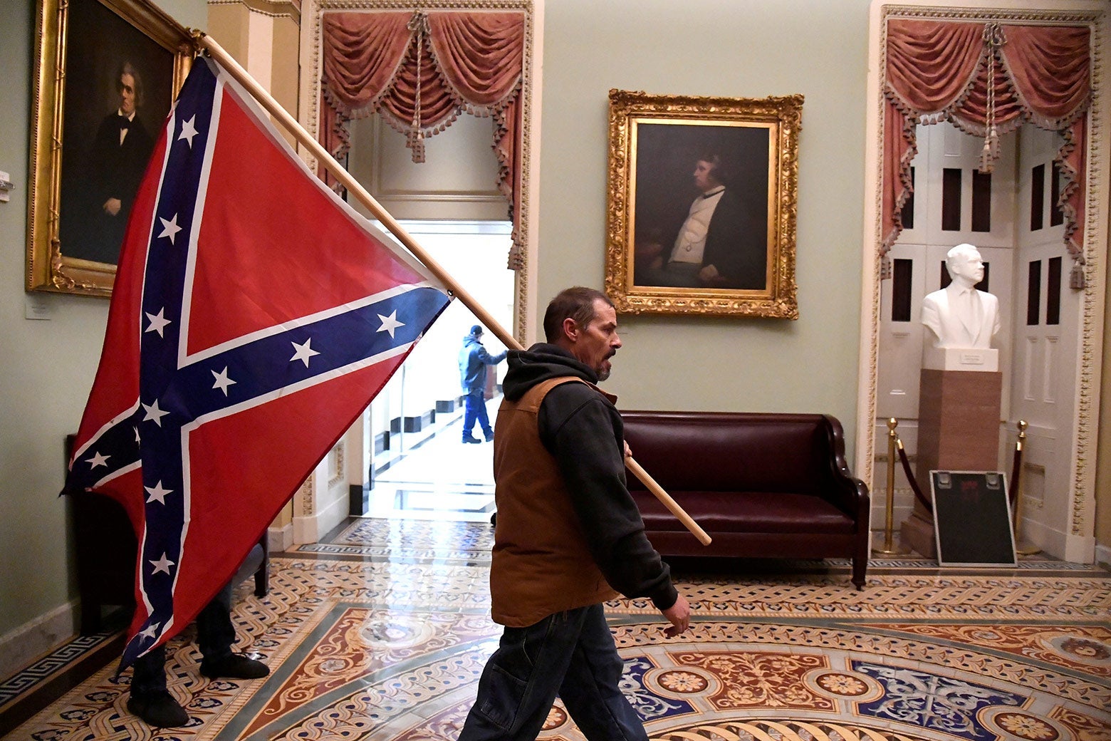 A man carries a Confederate flag over his shoulder.