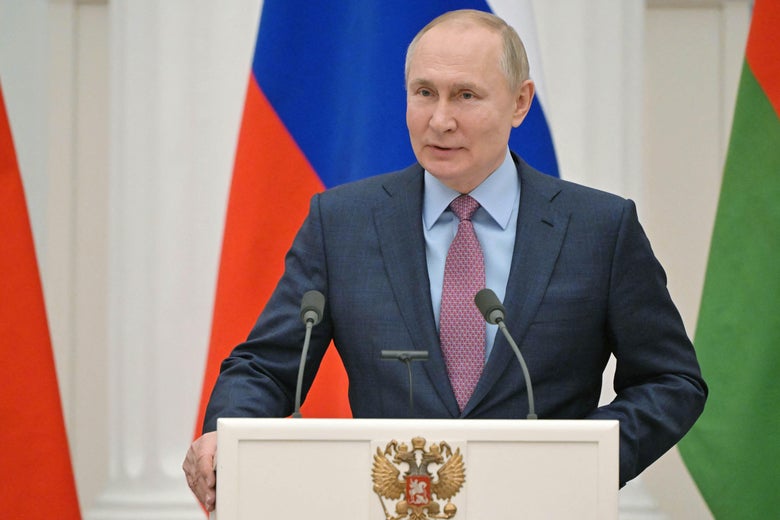 Putin stands with both hands on a lectern with a Russian flag behind him.