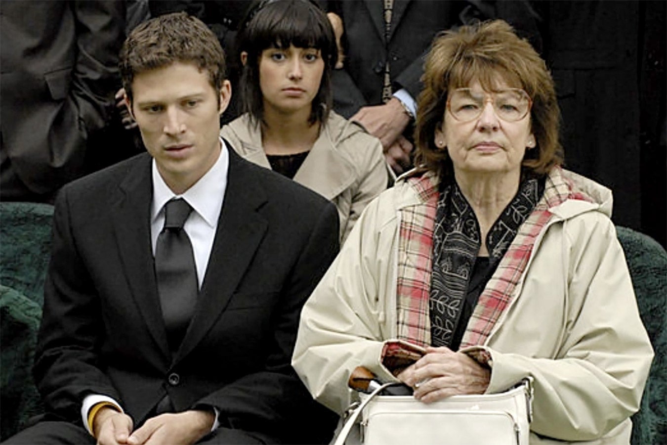 A teen boy and his grandmother look solemn at a funeral.
