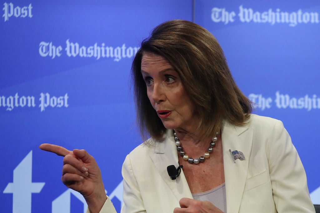 Pelosi, wearing a white suit coat, points to her right.