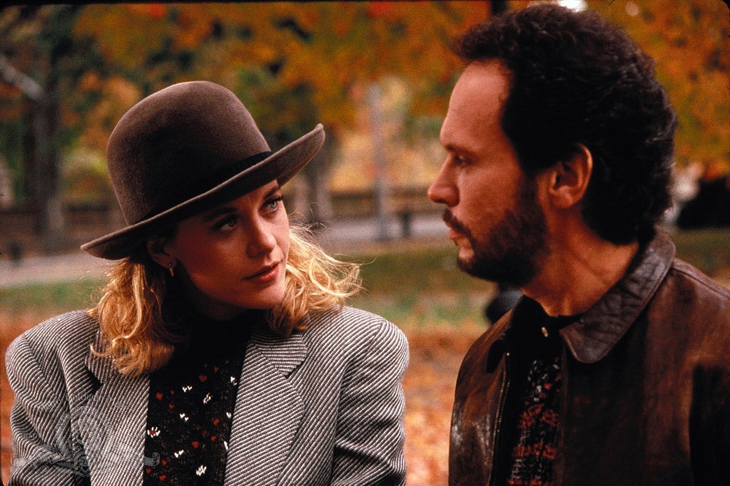Meg Ryan, wearing a large brown hat and a gray blazer, looks at Billy Crystal in profile.