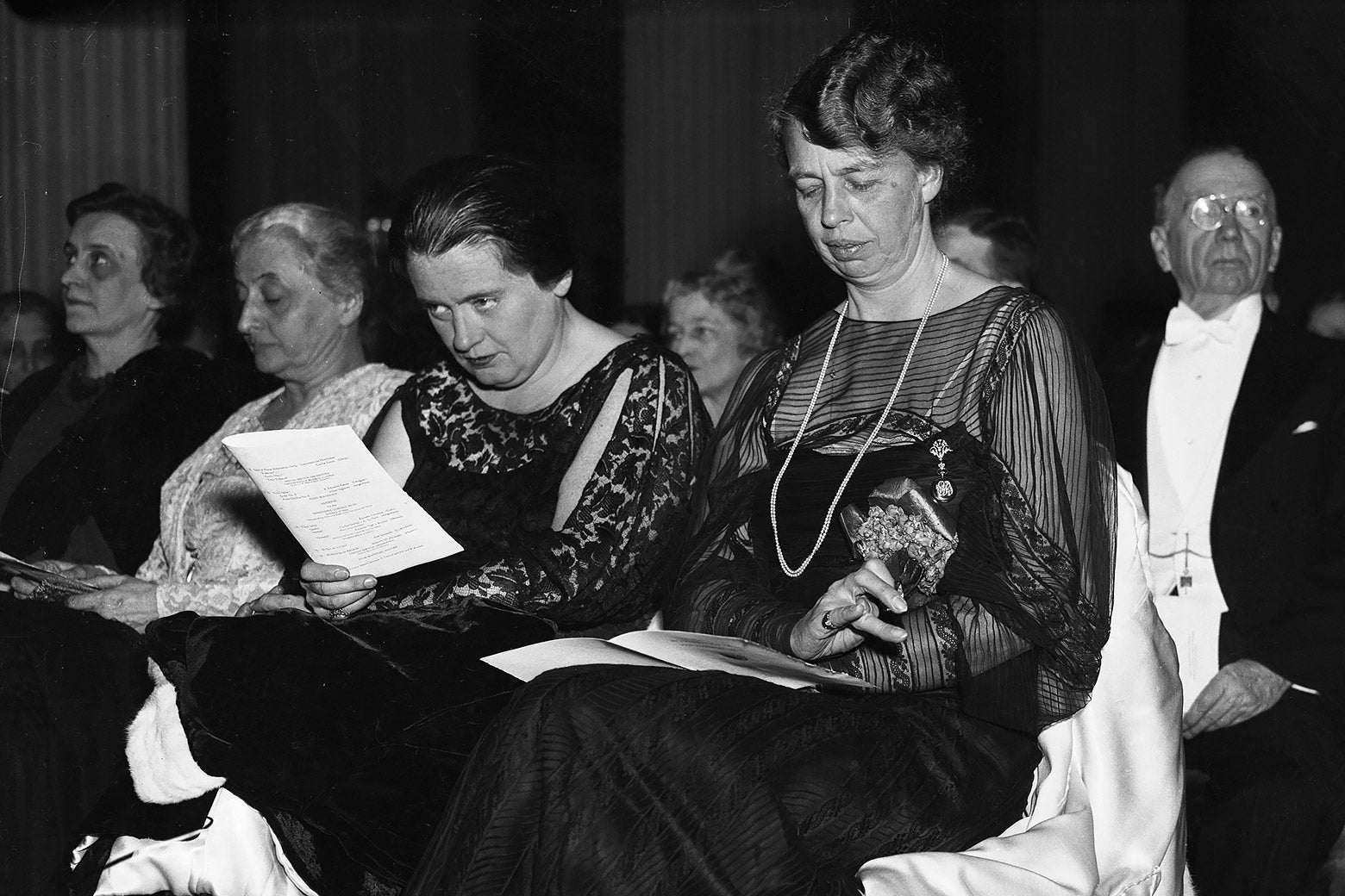 A black-and-white photo of Lorena Hickok and Eleanor Roosevelt wearing formalwear and sitting in an audience.