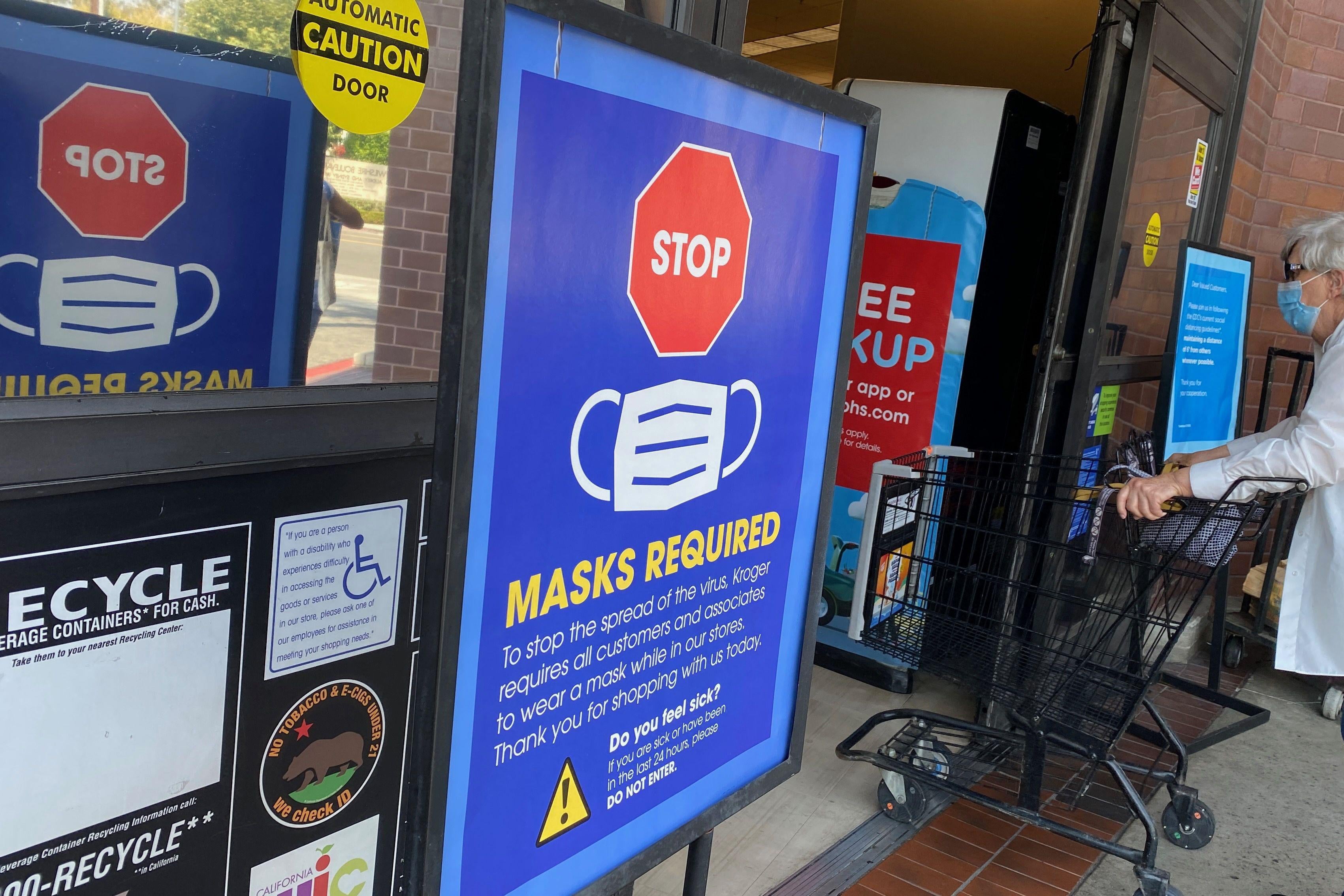 A shopper with a cart enters a store where it says, "Mask required" outside the doors.