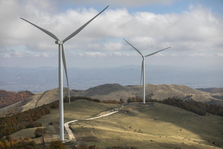 Two wind turbines are seen towering over grassy hills.